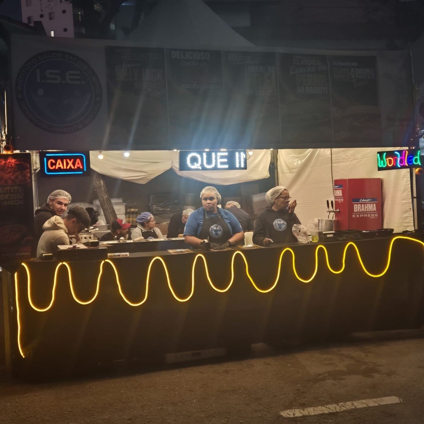 Equipe de touca e uniforme atendendo no balcão da barraca à noite
