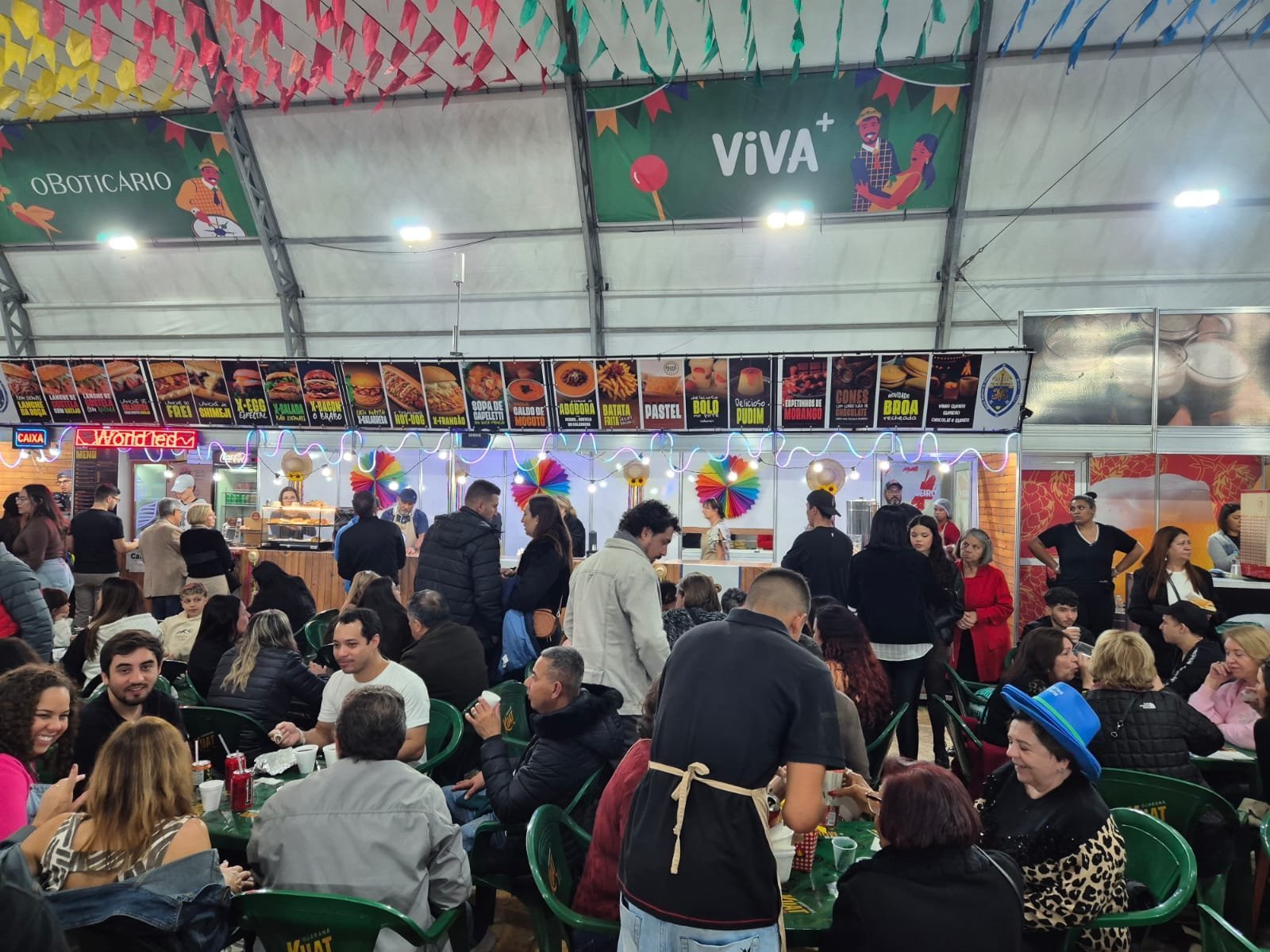 Praça de alimentação cheia sob as bandeirinhas da festa junina